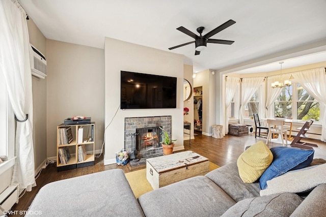 living room with wood finished floors, a fireplace, a wall mounted air conditioner, a baseboard radiator, and ceiling fan with notable chandelier
