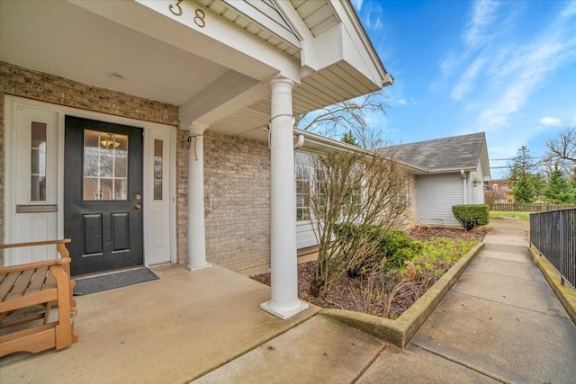 view of exterior entry featuring brick siding and fence