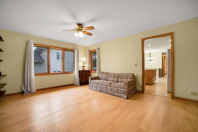 living room featuring baseboards, light wood-style flooring, and ceiling fan with notable chandelier
