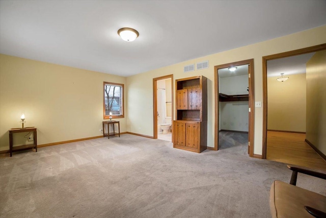 unfurnished bedroom with visible vents, baseboards, a spacious closet, ensuite bathroom, and light carpet