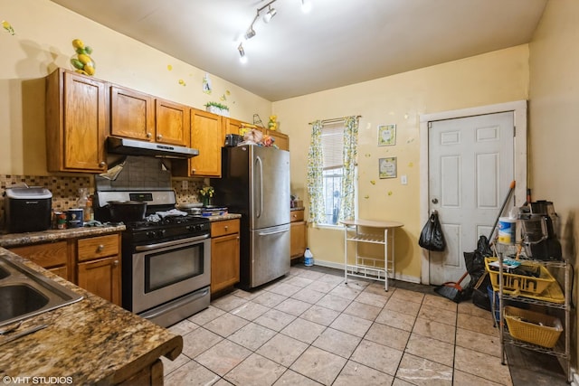 kitchen featuring brown cabinets, stainless steel appliances, backsplash, light tile patterned floors, and under cabinet range hood