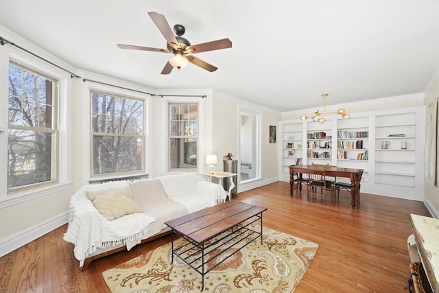 living area featuring baseboards, wood finished floors, and ceiling fan with notable chandelier