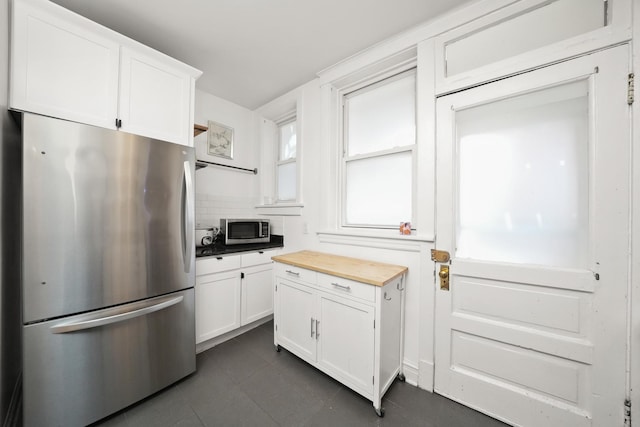 kitchen with white cabinetry, appliances with stainless steel finishes, butcher block counters, dark tile patterned flooring, and backsplash