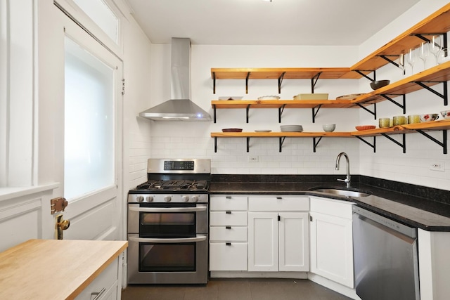 kitchen with tasteful backsplash, open shelves, a sink, stainless steel appliances, and wall chimney exhaust hood