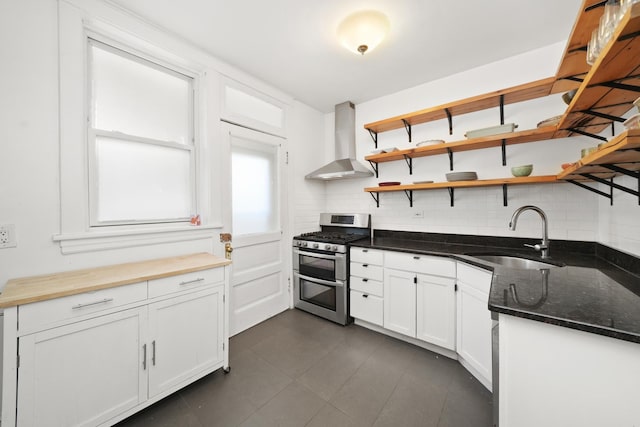 kitchen with a sink, wall chimney exhaust hood, backsplash, white cabinetry, and double oven range