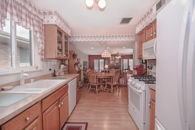 kitchen featuring visible vents, white appliances, light countertops, a sink, and light wood finished floors