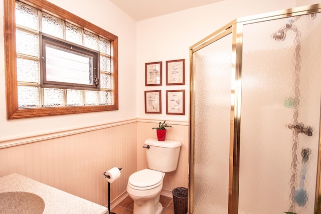 bathroom with tile patterned flooring, wainscoting, a stall shower, and toilet