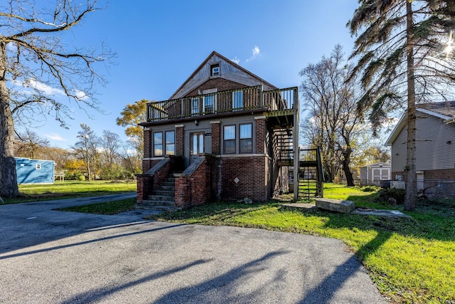 view of front of house featuring a front yard, stairs, a balcony, and brick siding