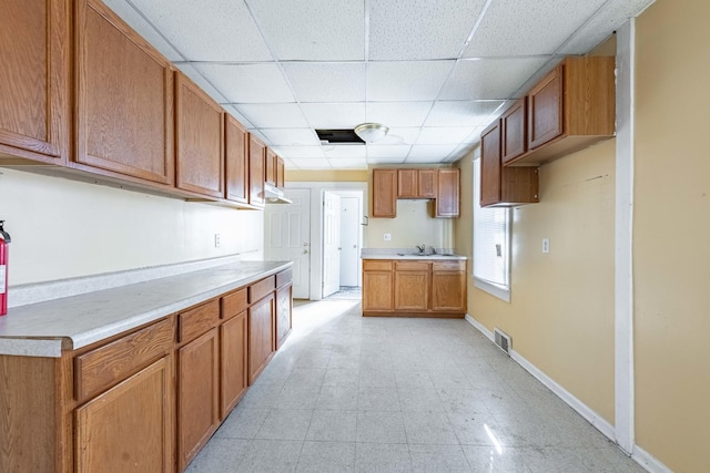 kitchen with visible vents, light countertops, baseboards, a paneled ceiling, and brown cabinetry