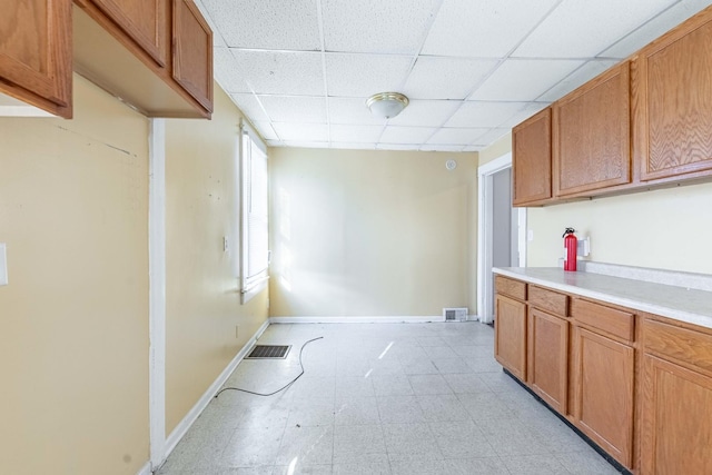 kitchen with light floors, a drop ceiling, light countertops, brown cabinets, and baseboards
