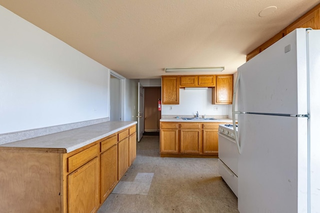 kitchen featuring light floors, white appliances, light countertops, brown cabinets, and a sink