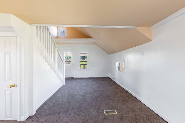additional living space with carpet flooring, stairs, visible vents, vaulted ceiling, and baseboards