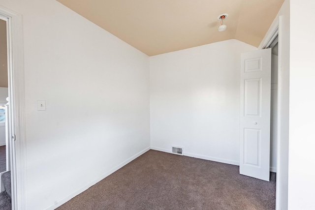 unfurnished room featuring baseboards, visible vents, dark colored carpet, and lofted ceiling
