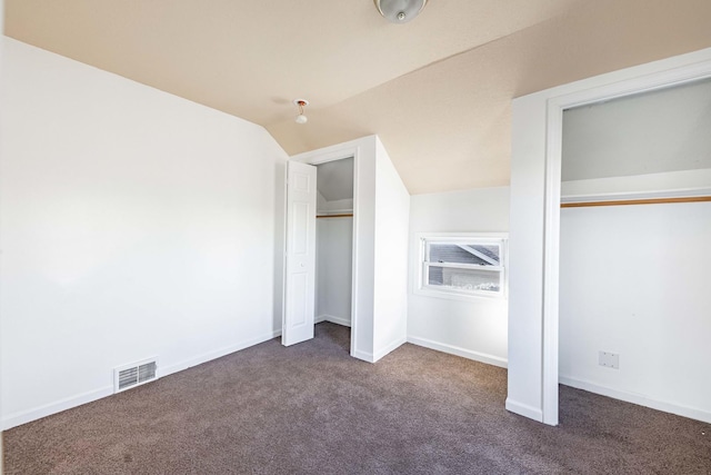 unfurnished bedroom featuring dark colored carpet, visible vents, baseboards, vaulted ceiling, and multiple closets