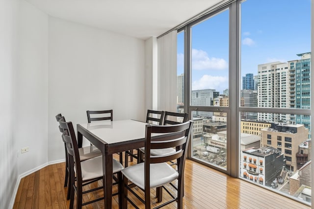 dining area featuring baseboards, a view of city, floor to ceiling windows, and hardwood / wood-style flooring