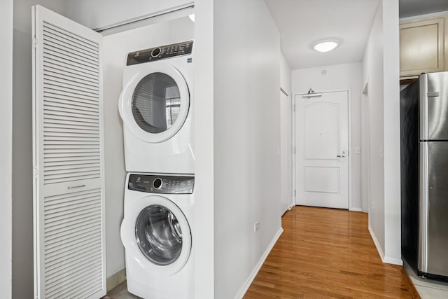 washroom featuring baseboards, stacked washer / drying machine, wood finished floors, and laundry area