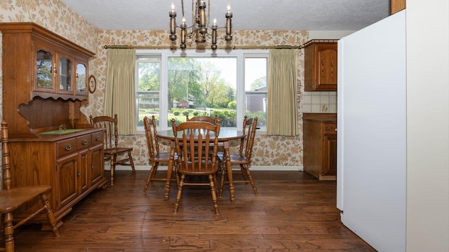dining room featuring a textured ceiling, baseboards, dark wood-type flooring, a notable chandelier, and wallpapered walls