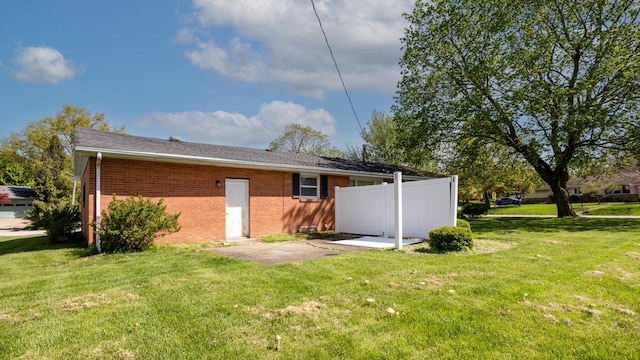 rear view of house featuring fence, brick siding, and a lawn