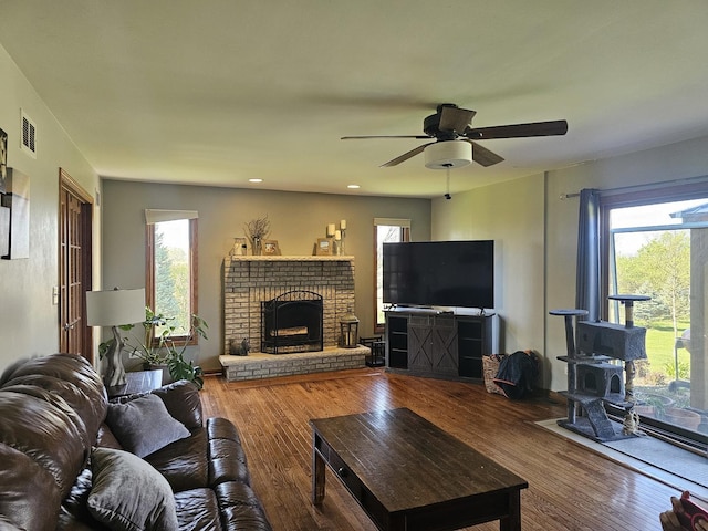 living area featuring a wood stove, a fireplace, a ceiling fan, visible vents, and wood finished floors