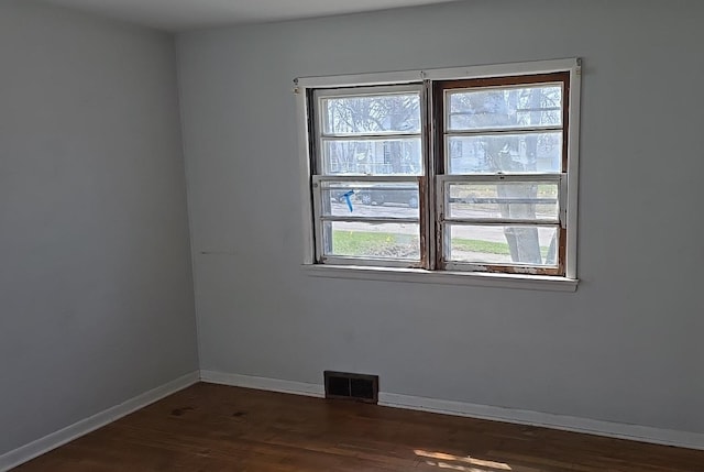 spare room featuring visible vents, baseboards, and dark wood finished floors
