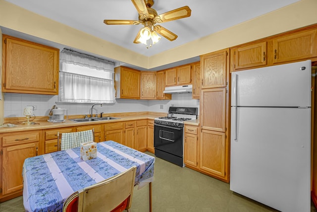 kitchen with a sink, light countertops, freestanding refrigerator, gas range, and under cabinet range hood