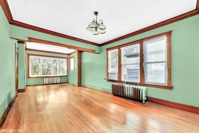 empty room with baseboards, ornamental molding, radiator, and a notable chandelier