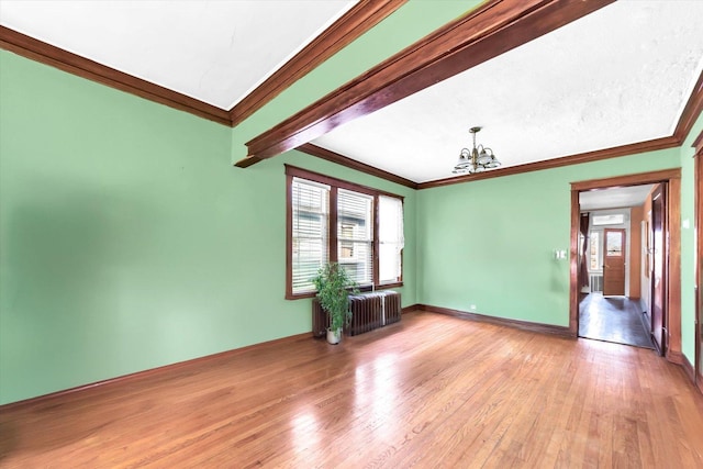 empty room with crown molding, a notable chandelier, radiator, and hardwood / wood-style floors