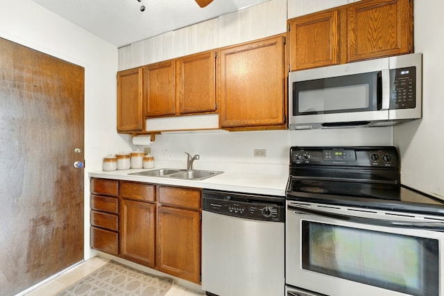 kitchen with a sink, brown cabinetry, light countertops, and appliances with stainless steel finishes