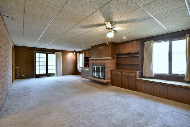 unfurnished living room with carpet floors, a ceiling fan, a fireplace, and wood walls
