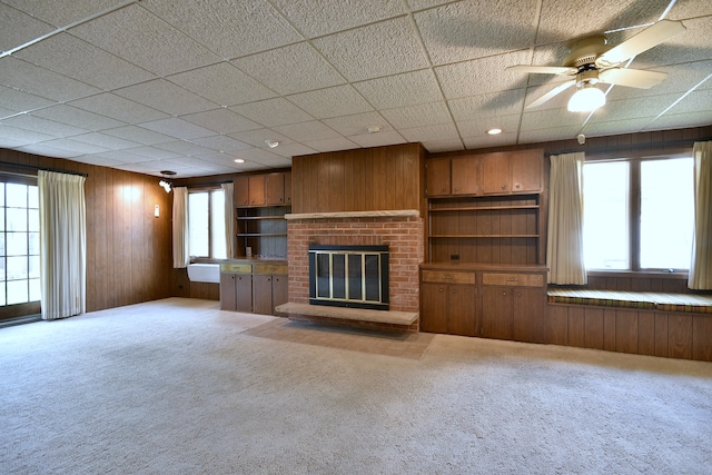 unfurnished living room with wood walls, a drop ceiling, carpet, and a fireplace