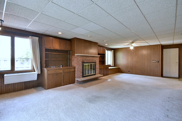 unfurnished living room with carpet floors, wood walls, a brick fireplace, and a ceiling fan
