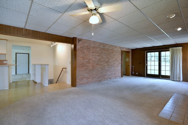 interior space featuring a ceiling fan, carpet flooring, a drop ceiling, and brick wall