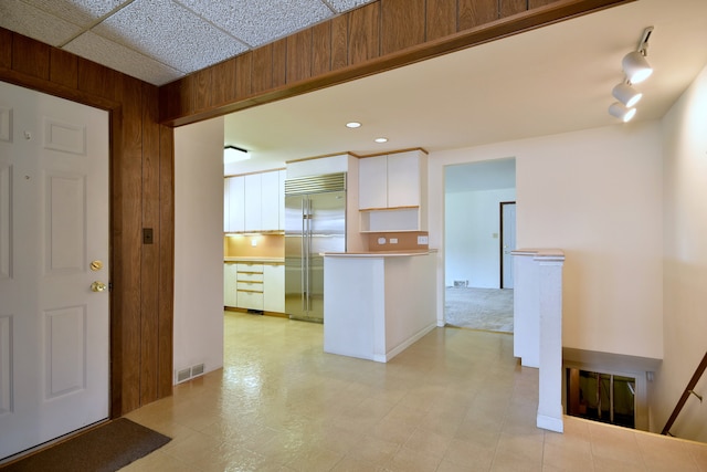 kitchen featuring visible vents, a peninsula, wooden walls, built in refrigerator, and white cabinets