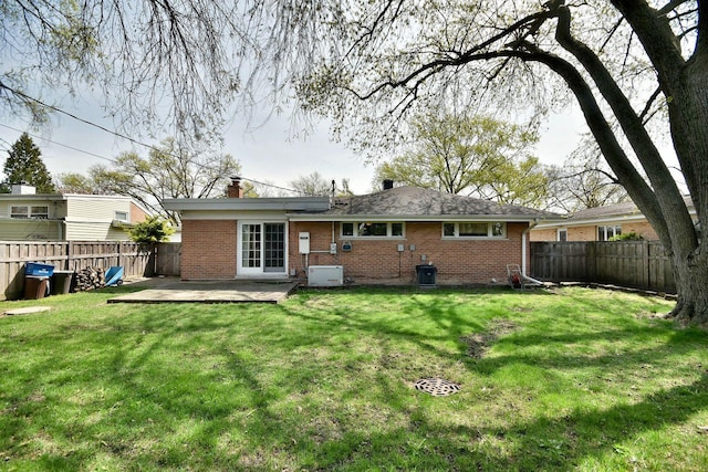 back of property featuring brick siding, a fenced backyard, a lawn, and a chimney