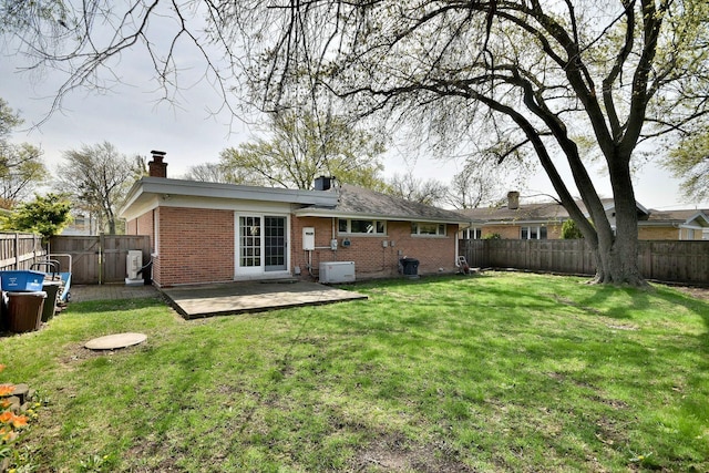 back of property with a yard, brick siding, a chimney, and a fenced backyard