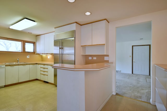 kitchen with white dishwasher, open shelves, a sink, light countertops, and a peninsula
