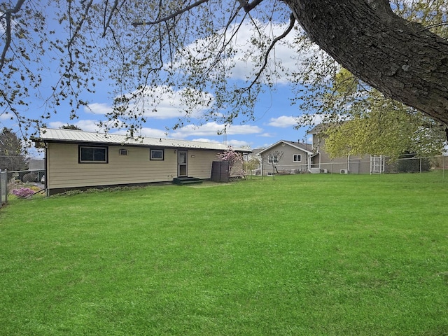 rear view of house featuring a fenced backyard, entry steps, a yard, and metal roof