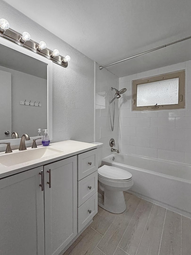 full bath with wood finished floors, vanity, toilet, a textured wall, and tub / shower combination