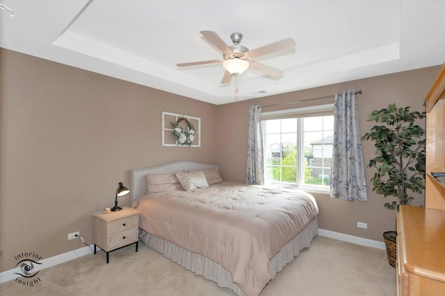 bedroom featuring baseboards, ceiling fan, light carpet, and a tray ceiling