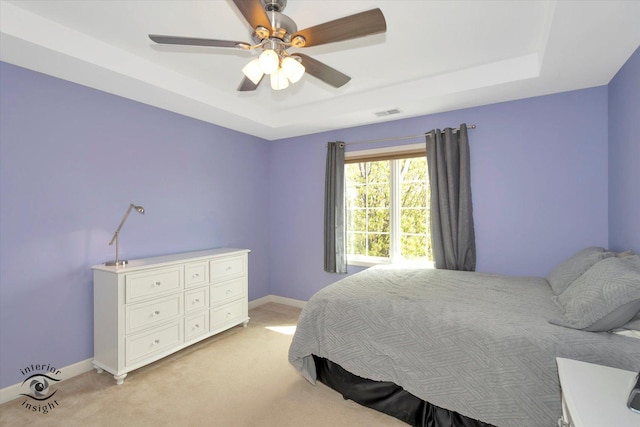 bedroom featuring light colored carpet, baseboards, and a tray ceiling