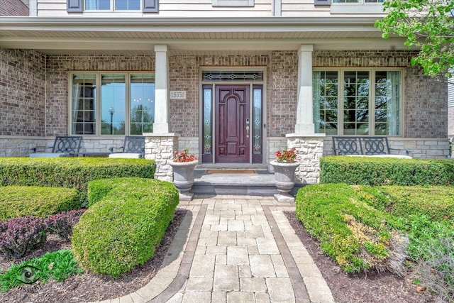 entrance to property featuring a porch, brick siding, and stone siding