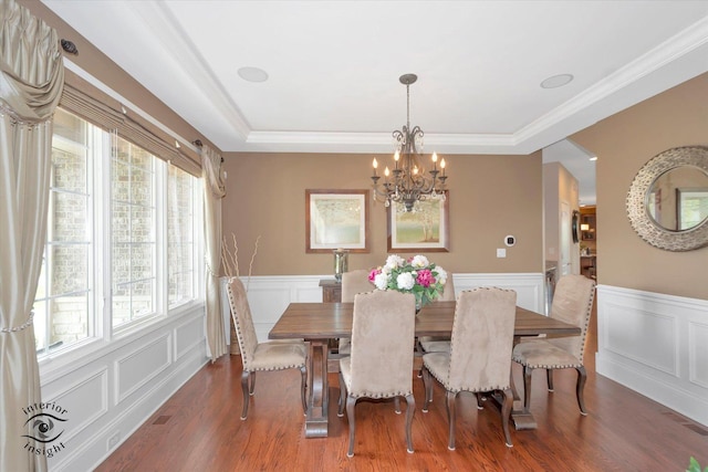 dining area featuring an inviting chandelier, wainscoting, a decorative wall, and wood finished floors