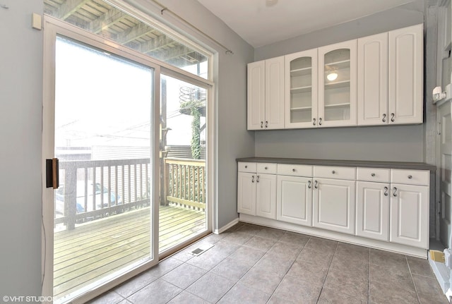 interior space featuring dark countertops, white cabinetry, baseboards, glass insert cabinets, and light tile patterned flooring