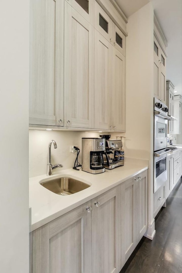 kitchen with dark wood-style flooring, glass insert cabinets, light countertops, stainless steel double oven, and a sink