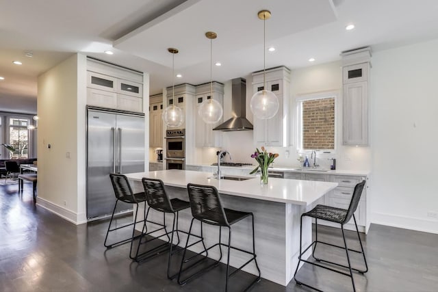 kitchen featuring wall chimney range hood, baseboards, appliances with stainless steel finishes, and a center island with sink