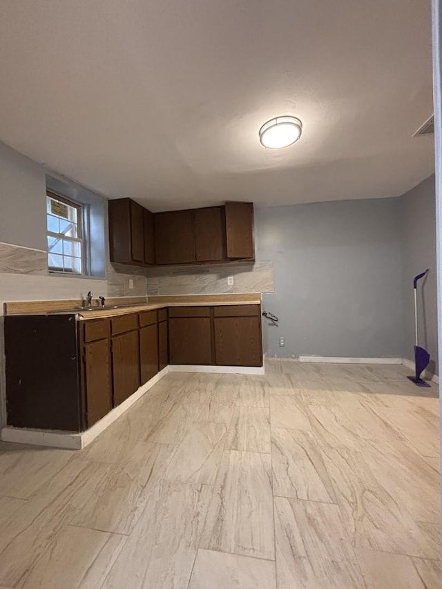 kitchen with a sink, light countertops, baseboards, and dark brown cabinetry