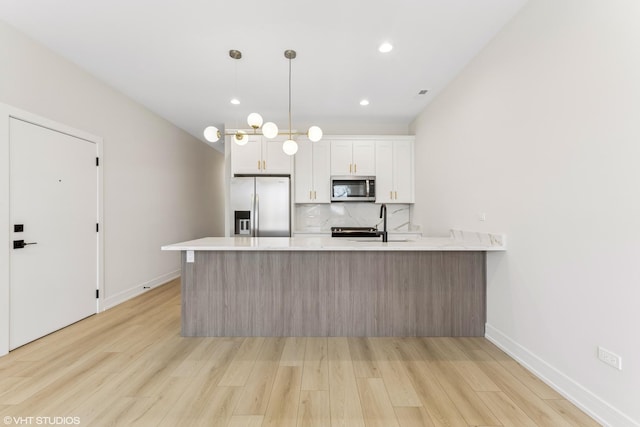 kitchen with a peninsula, light wood-type flooring, light countertops, backsplash, and stainless steel appliances