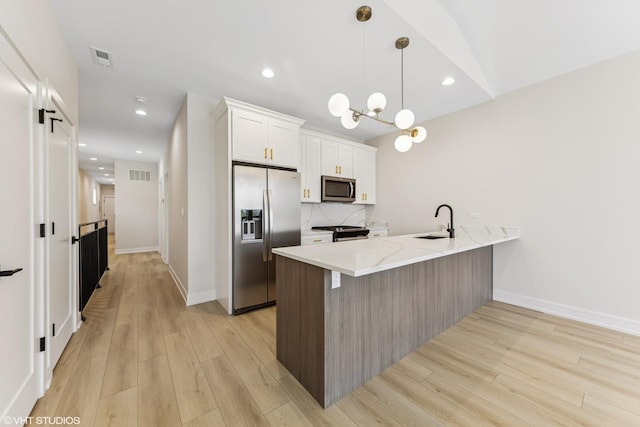 kitchen with visible vents, a peninsula, light wood-style floors, a sink, and appliances with stainless steel finishes