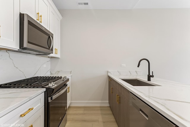 kitchen featuring appliances with stainless steel finishes, a sink, white cabinetry, light wood-type flooring, and visible vents