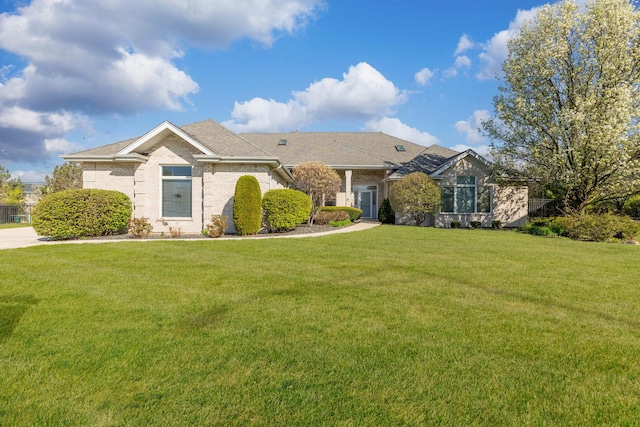 ranch-style home featuring brick siding, a front yard, and roof with shingles
